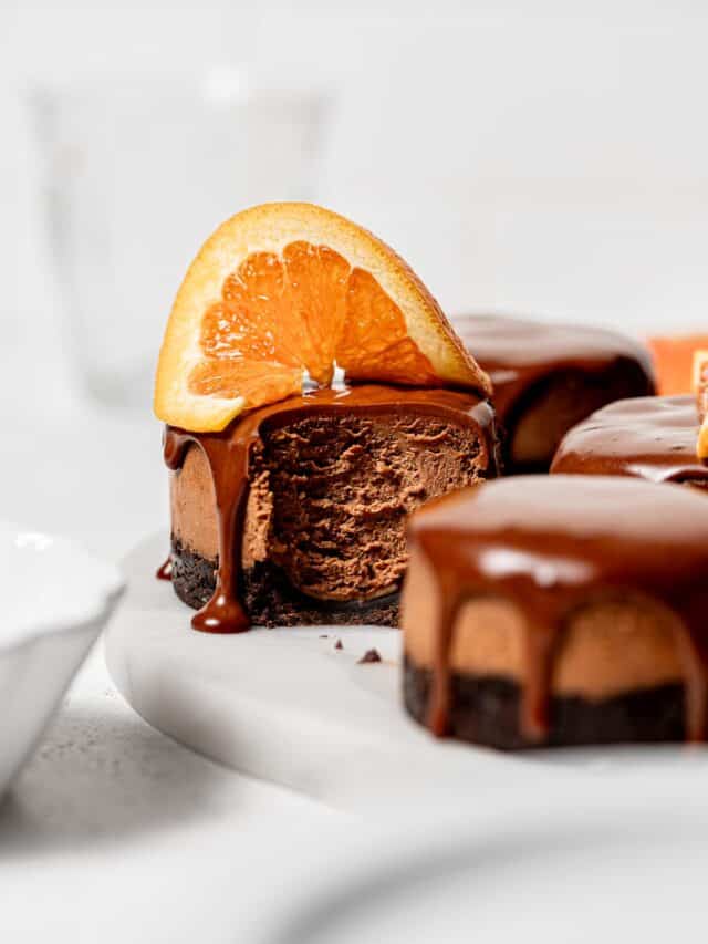 mini chocolate orange cheesecakes with orange slices on marble slab.