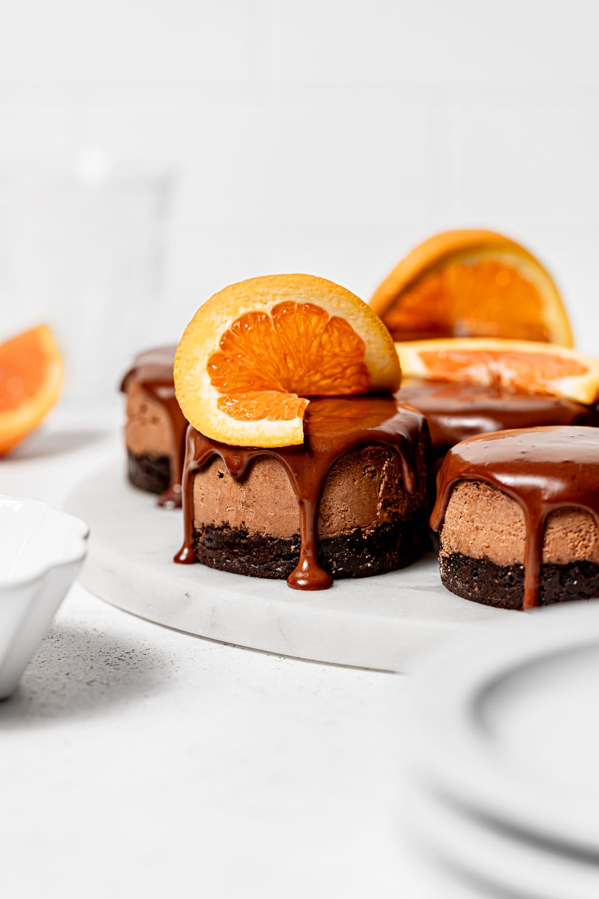 mini chocolate orange cheesecakes with orange slices on marble slab.