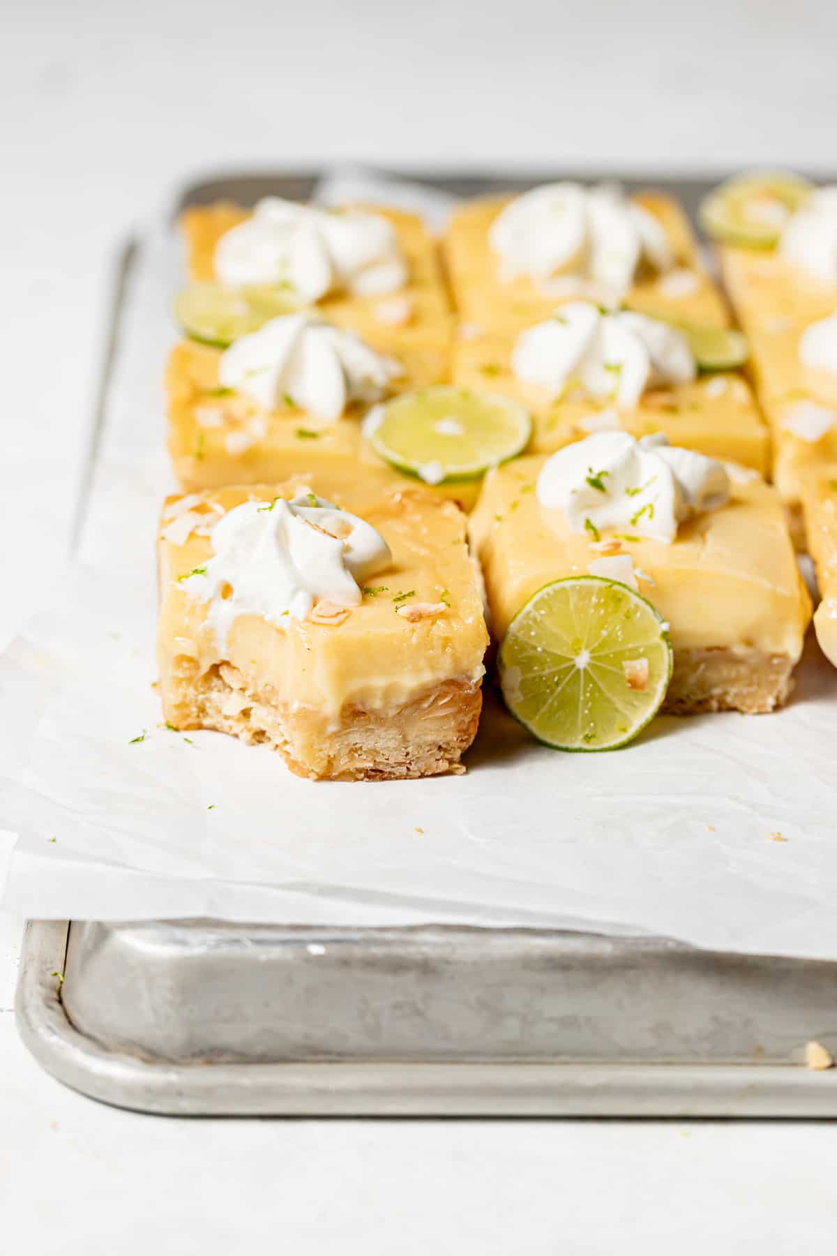 coconut key lime bars with dollops of whipped cream on baking tray with bite taken out of one.