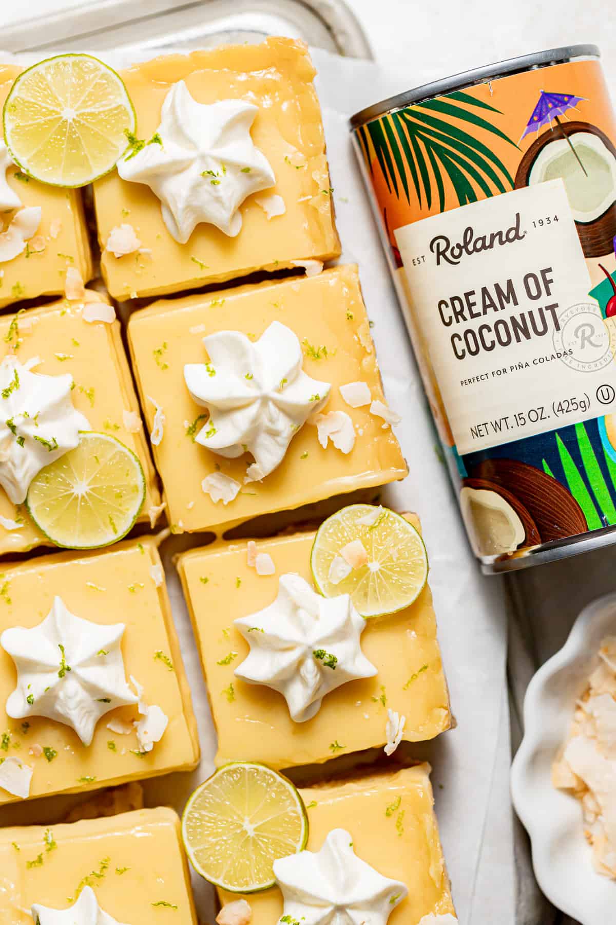 coconut key lime bars with dollops of whipped cream next to jar of Roland cream of coconut.