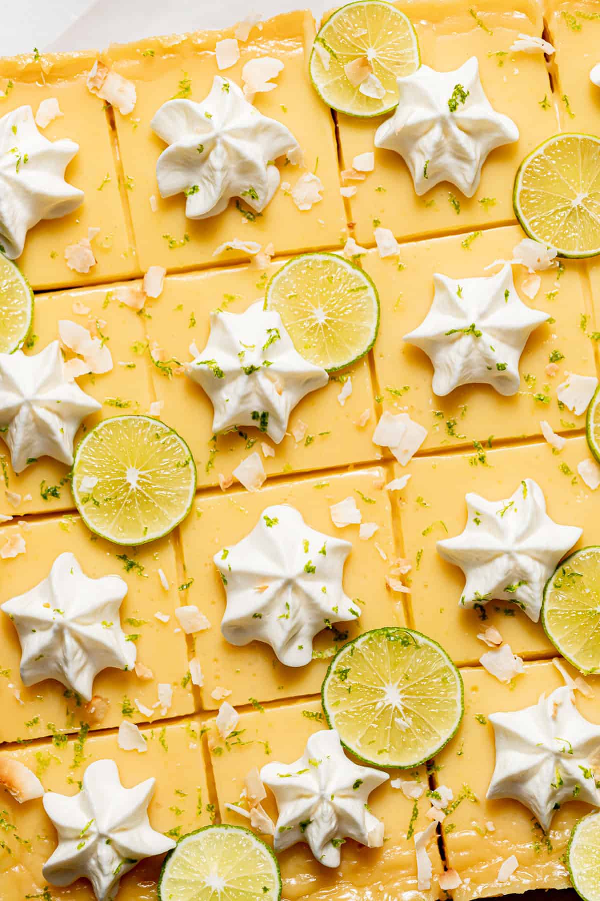 coconut key lime bars with dollops of whipped cream and lime slices.