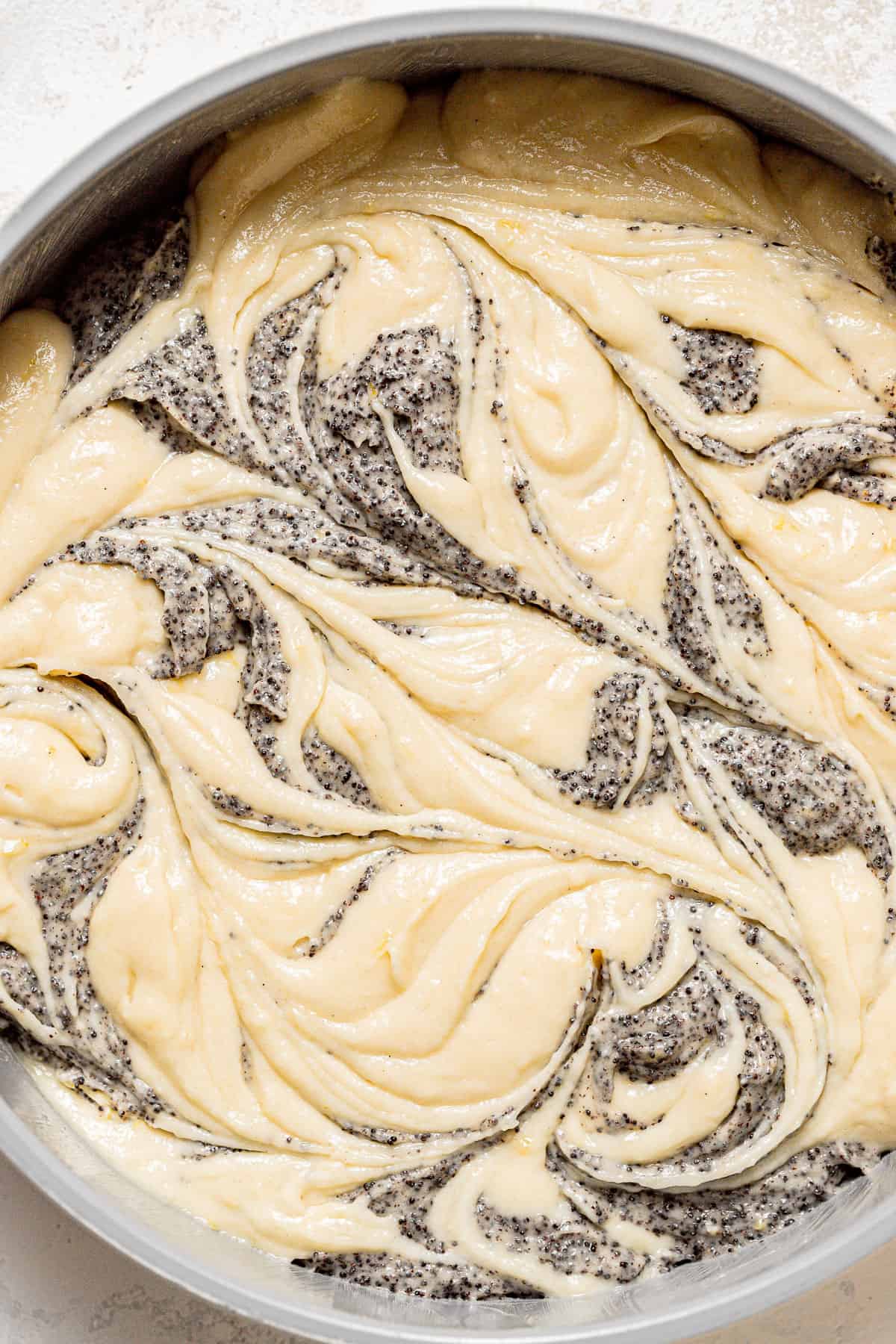 cake batter and poppy seeds swirled in cake pan.