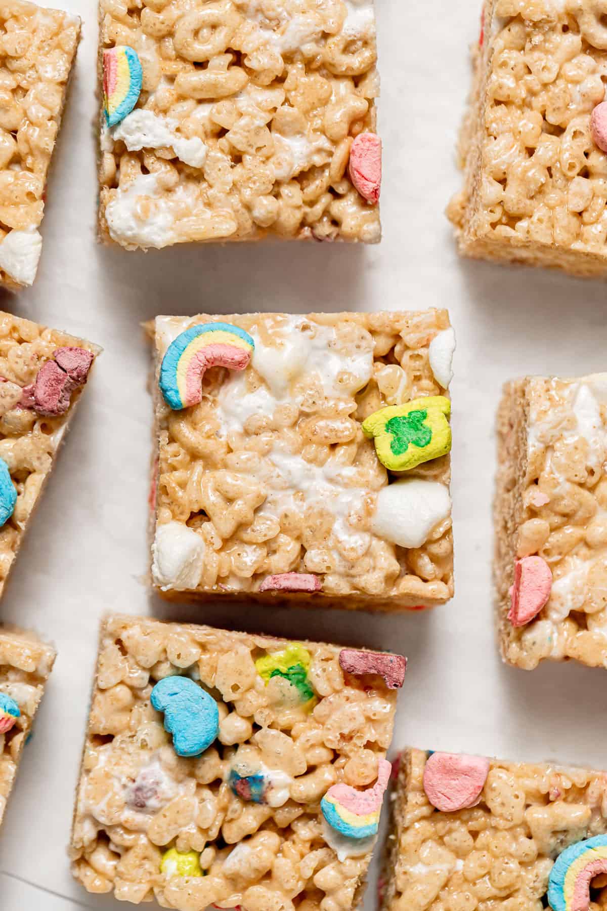 Lucky Charms Rice Krispie Treats cut into squares spread out on parchment paper.