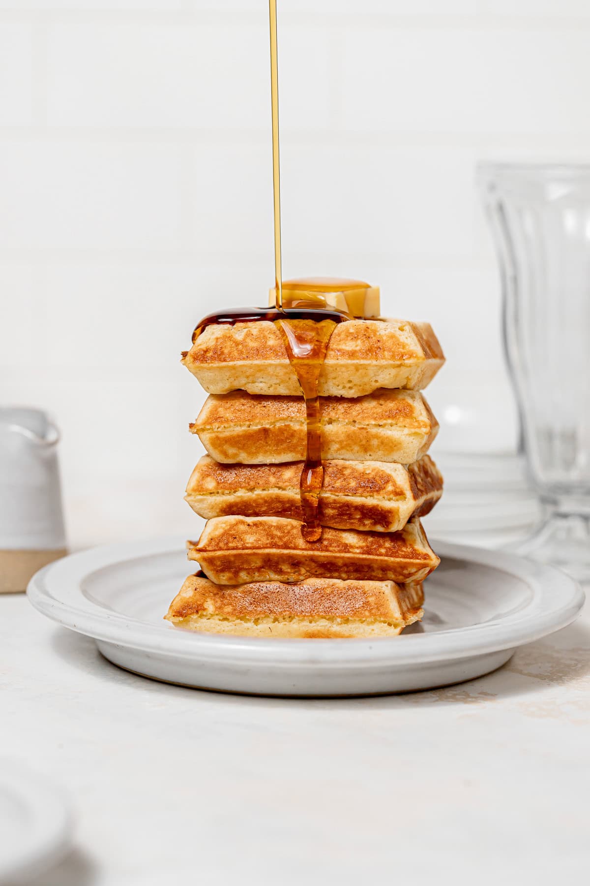 yeasted belgian waffles stacked with maple syrup being poured on top.