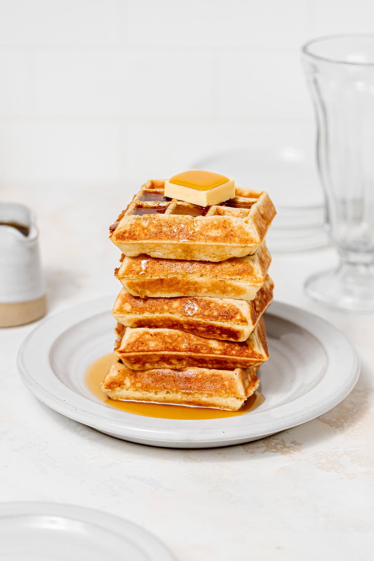 yeasted belgian waffles stacked with maple syrup and butter on top.