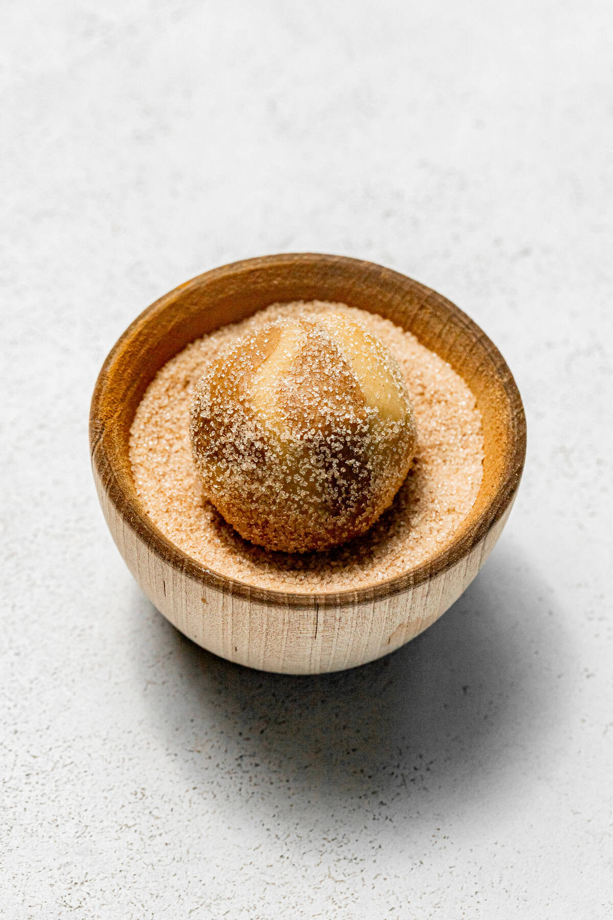 cookie dough ball in bowl of spiced sugar.