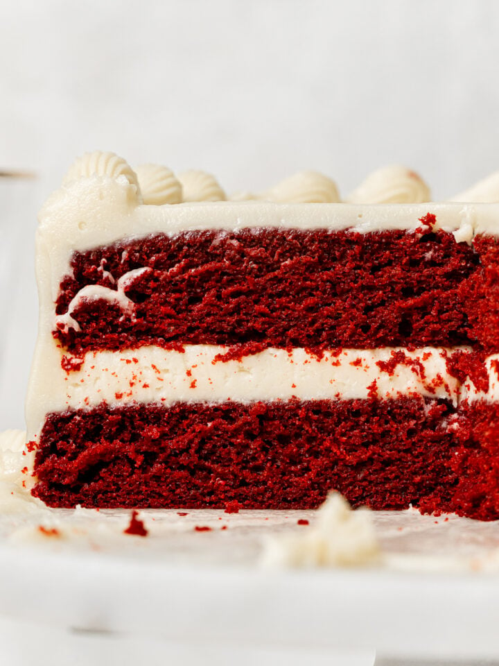 red velvet cake with cream cheese frosting on marble cake stand.