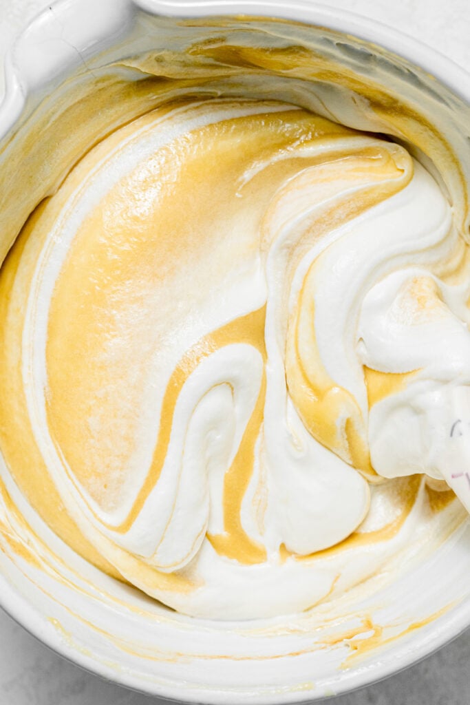 A bowl of whipped cream folded into pastry cream with a spoon in it.