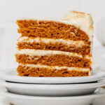 slice of pumpkin cake with cream cheese frosting on stacked plates.