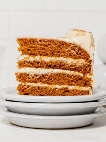 slice of pumpkin cake with cream cheese frosting on stacked plates.