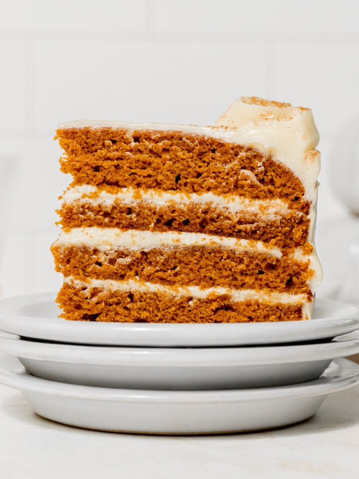 slice of pumpkin cake with cream cheese frosting on stacked plates.