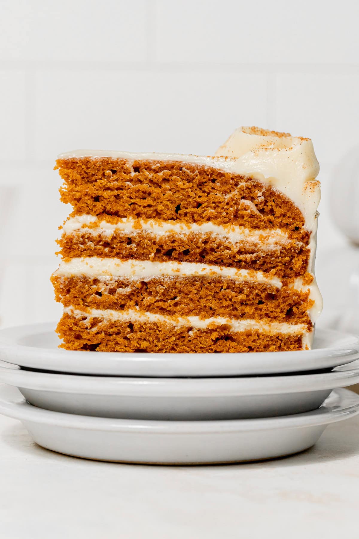 slice of pumpkin cake with cream cheese frosting on stacked plates.
