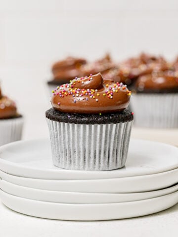 chocolate birthday cupcake on stack of white plates.