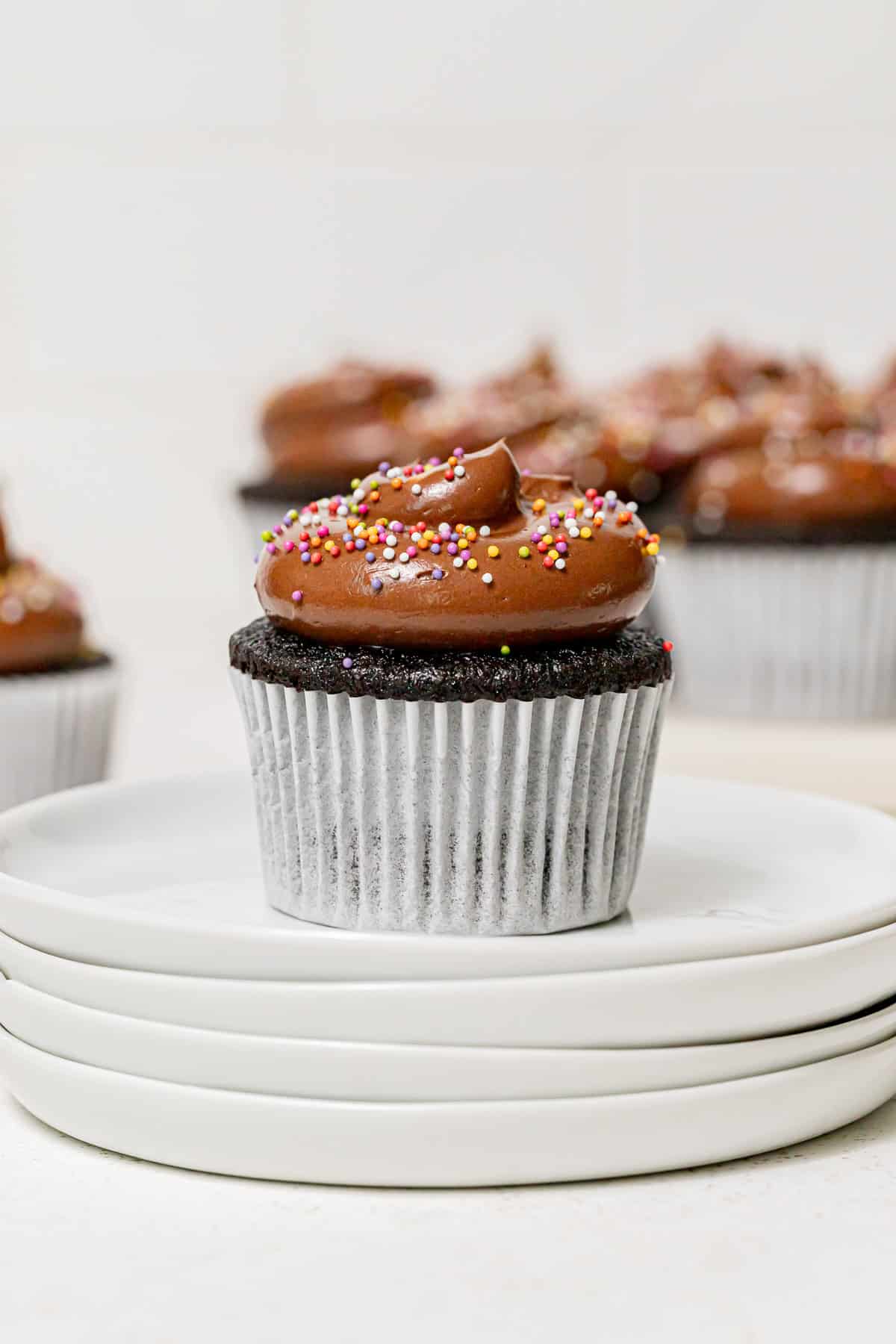 chocolate birthday cupcake on stack of white plates.