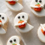 white ghost cupcakes holding candy pumpkins on parchment paper.