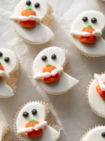 white ghost cupcakes holding candy pumpkins on parchment paper.
