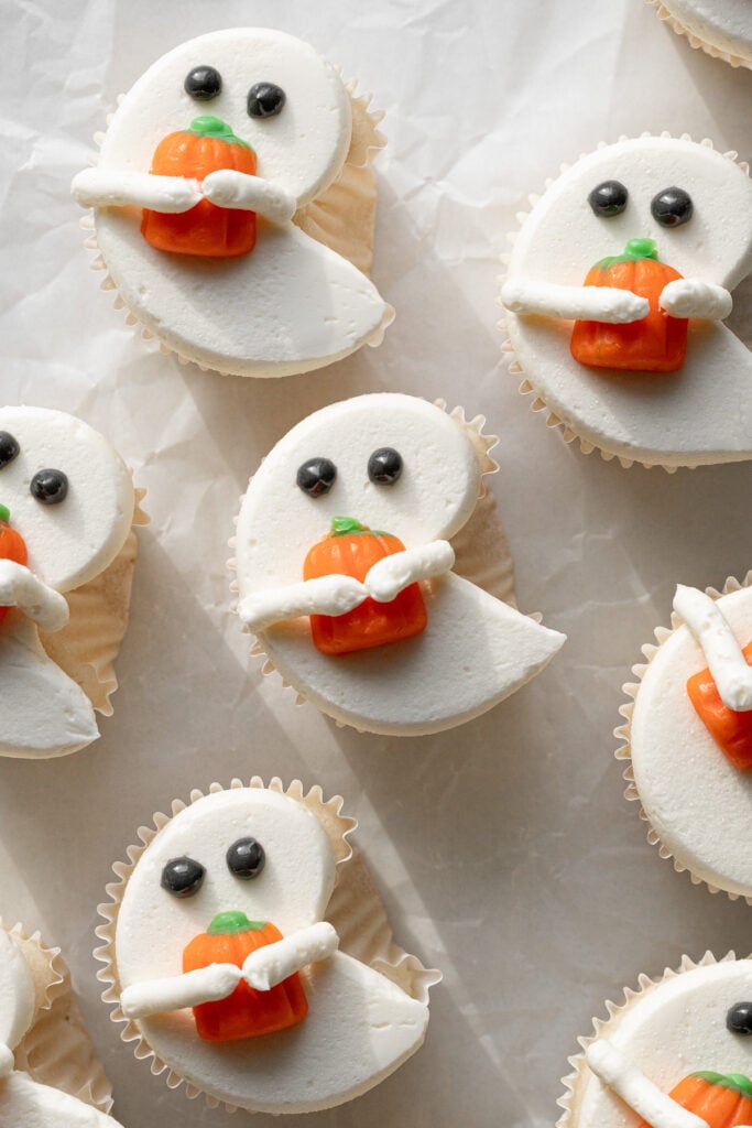 white ghost cupcakes holding candy pumpkins on parchment paper.