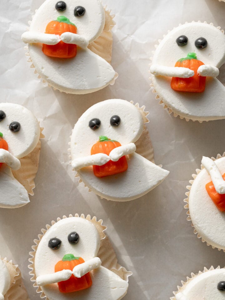 white ghost cupcakes holding candy pumpkins on parchment paper.
