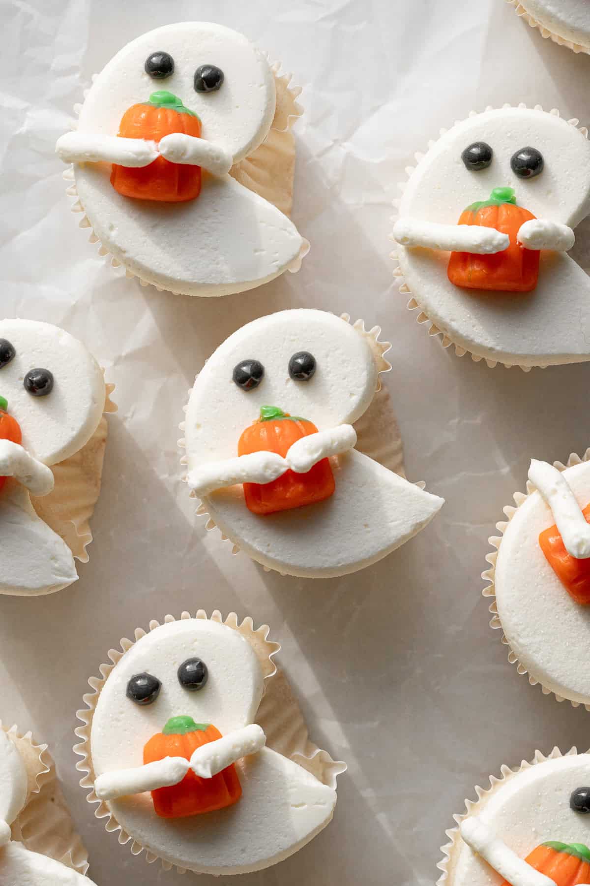 white ghost cupcakes holding candy pumpkins on parchment paper.