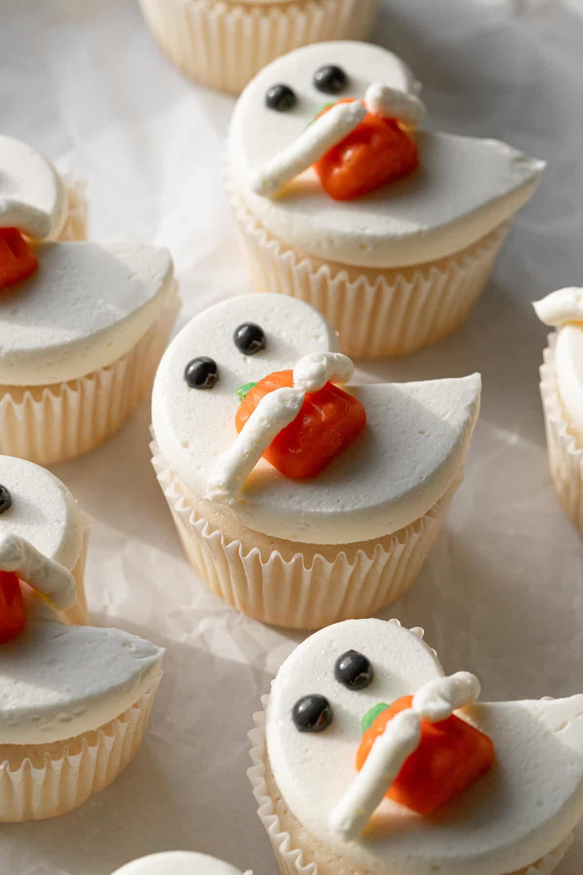 angled view of White Ghost Cupcakes on parchment.