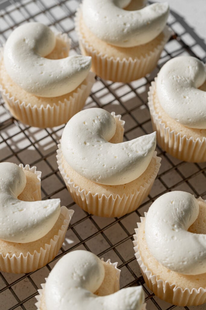 baked cupcakes with buttercream on wire rack.