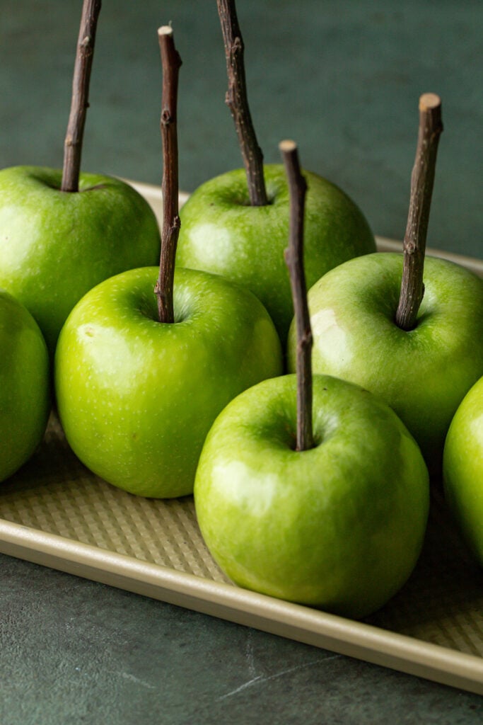 Granny Smith apples with apple sticks inserted at their tops.