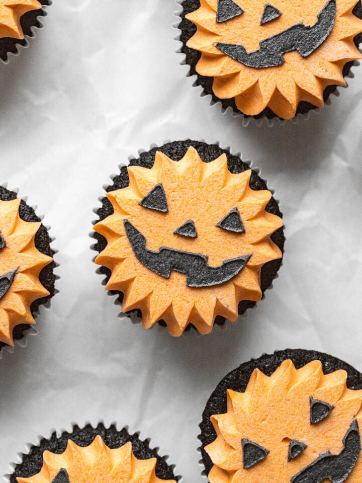 black velvet jack-o'-lantern cupcakes on parchment paper.