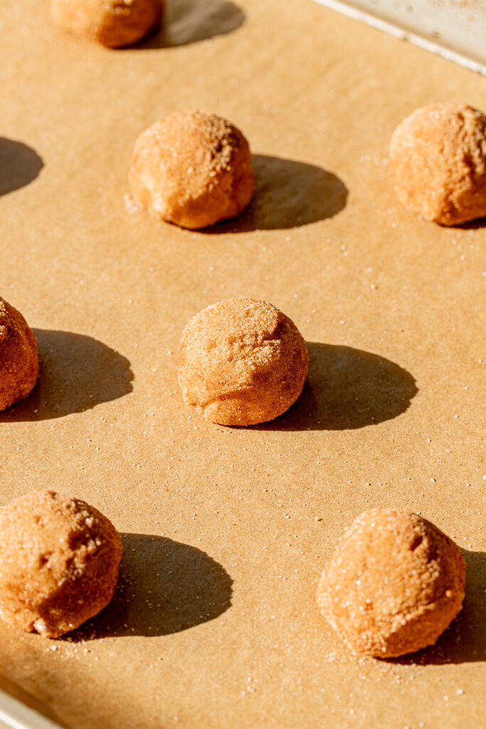 cookie dough balls rolled in cinnamon sugar on baking sheet.