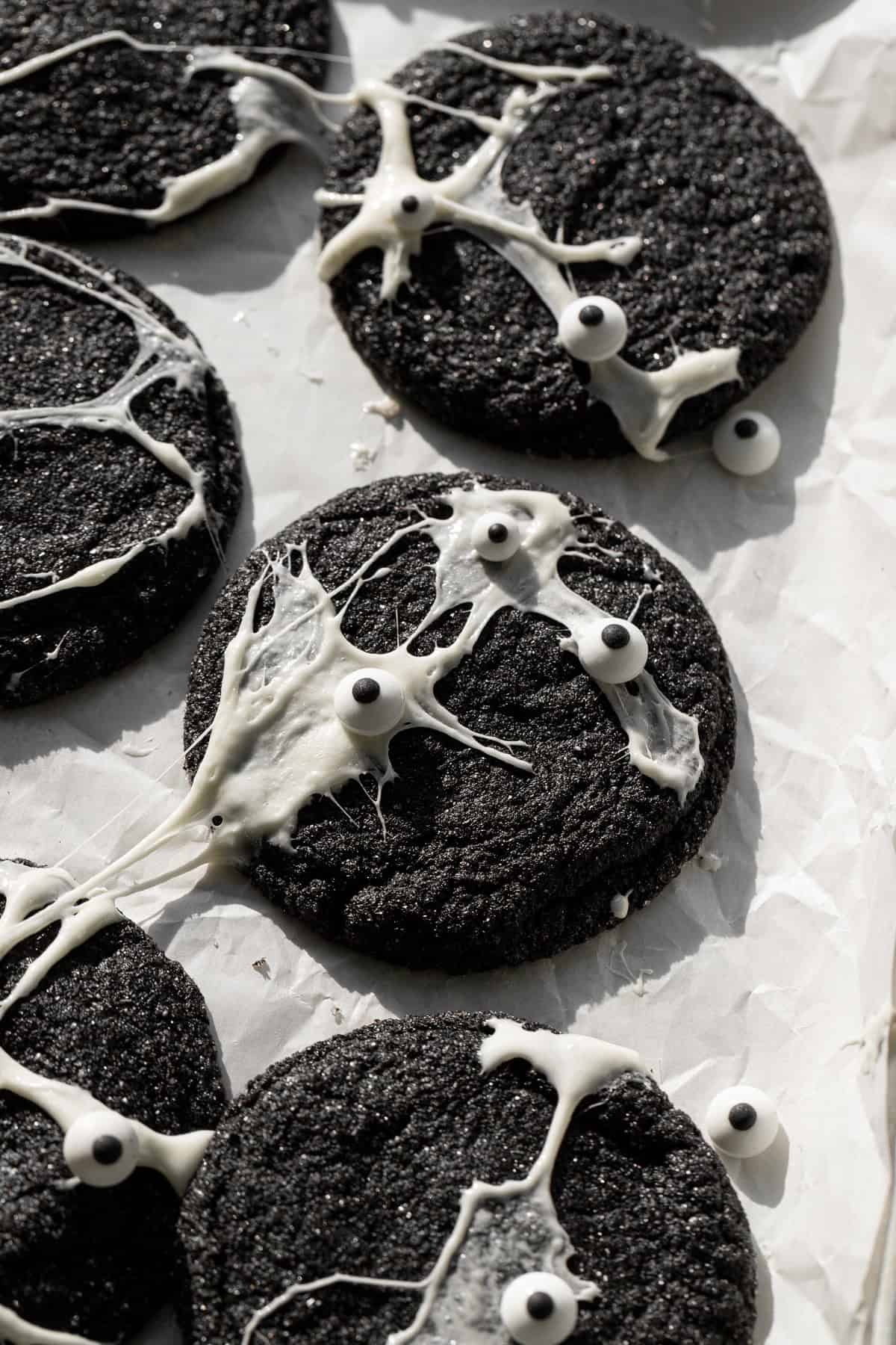 Spiderweb Black Velvet Cheesecake Cookies with candy eyes on parchment paper.